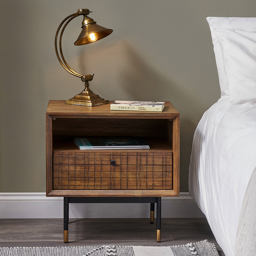 Shop the Arte Bedside Unit in dark brown acacia wood with etched detailing and sleek black metal legs, one drawer and open niche offer ample storage for essentials. Shop online today at www.nobleandnook.co.uk