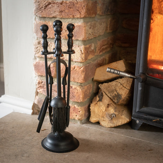Black fireplace tool set in front of a brick fireplace with logs.