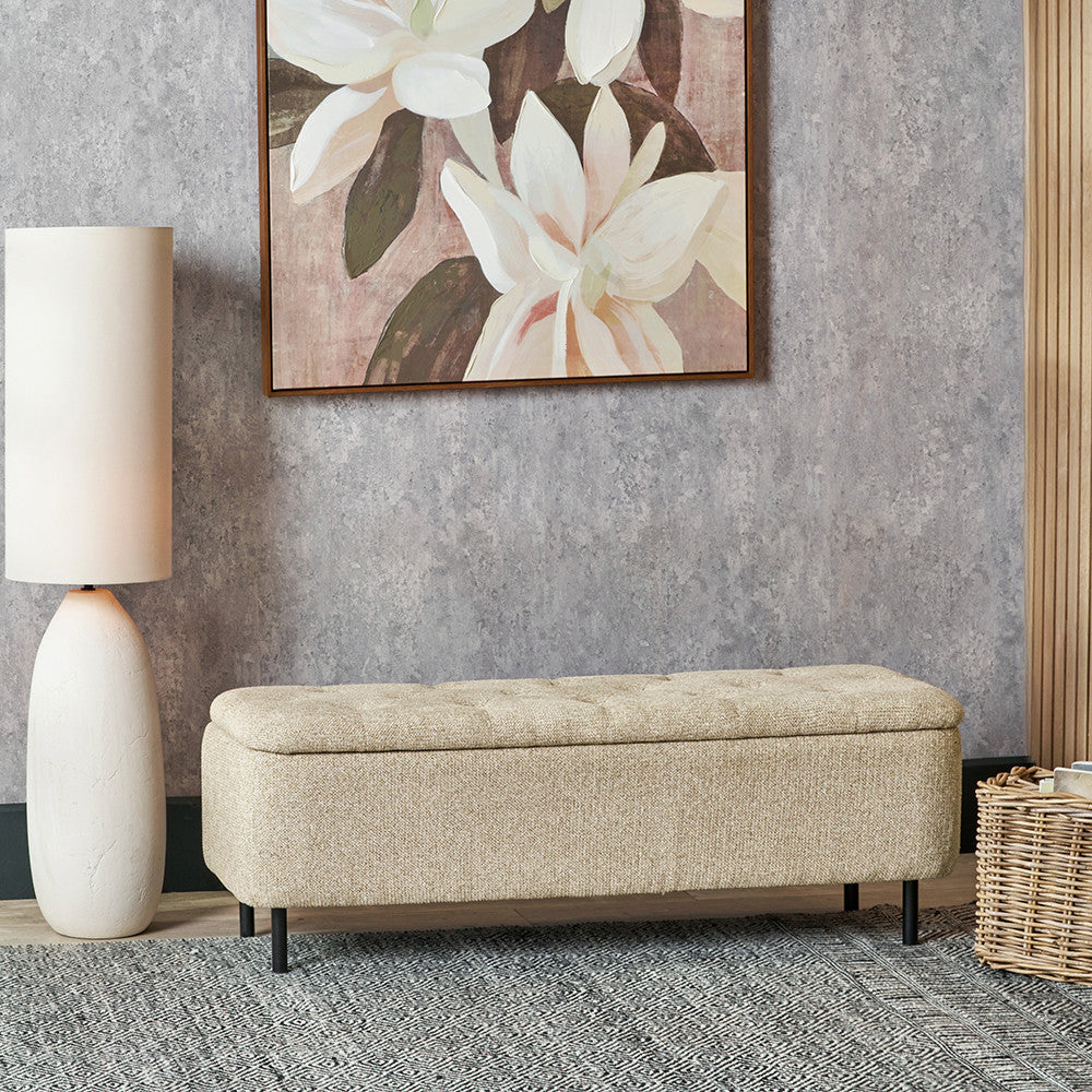 Beige storage bench in a room with a floral painting and lamp.