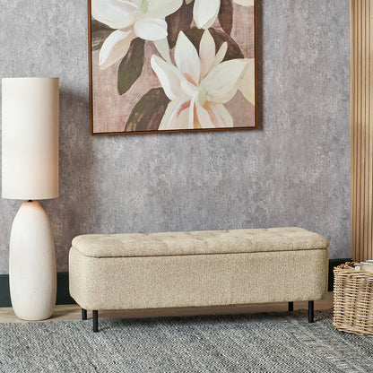 Beige storage bench in a room with a floral painting and lamp.