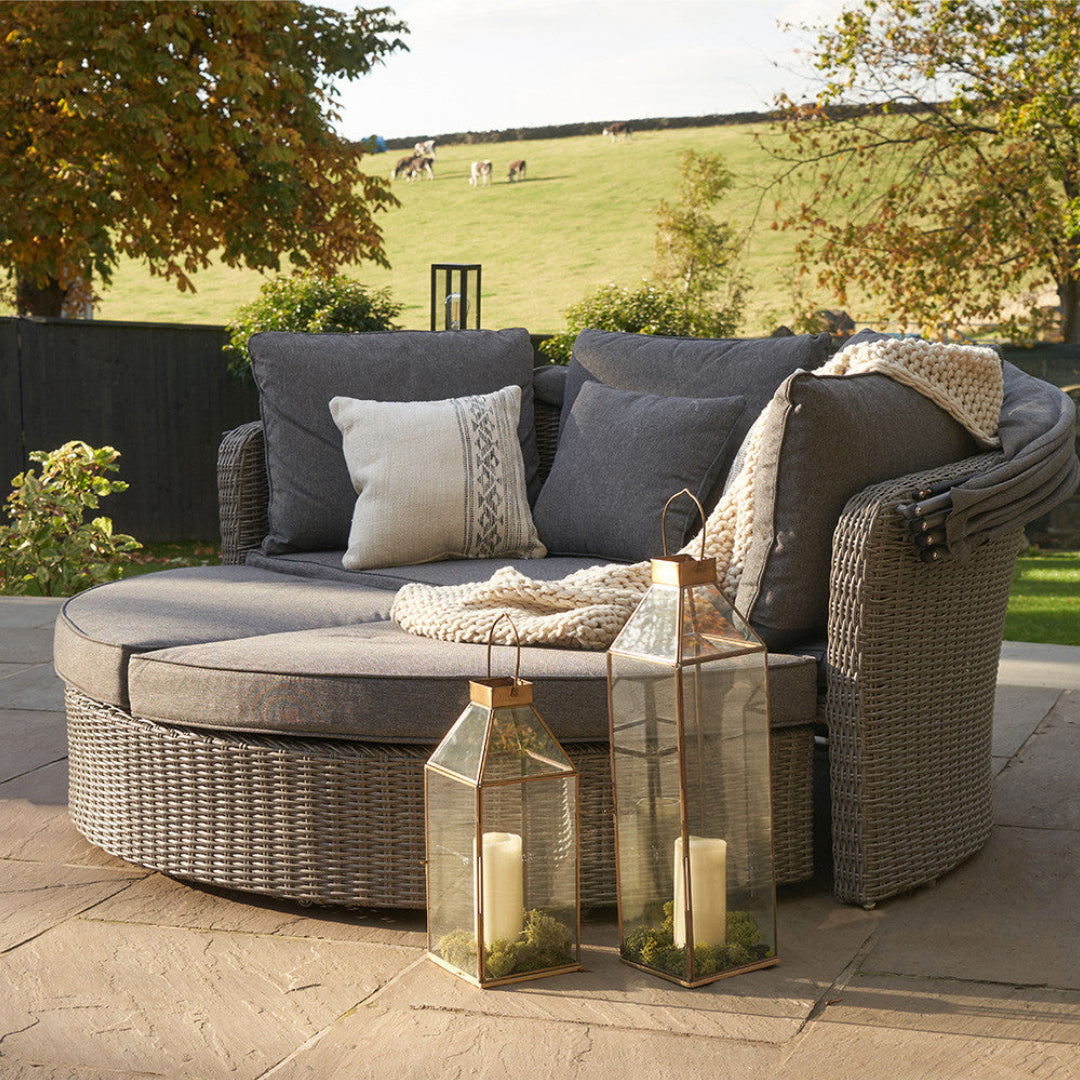 Outdoor patio set with cushions and lanterns on a stone patio with a scenic background.