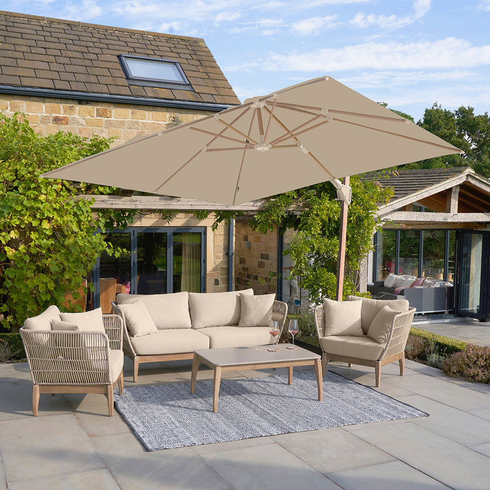 Outdoor patio set with beige furniture, umbrella, and rug on a stone patio.
