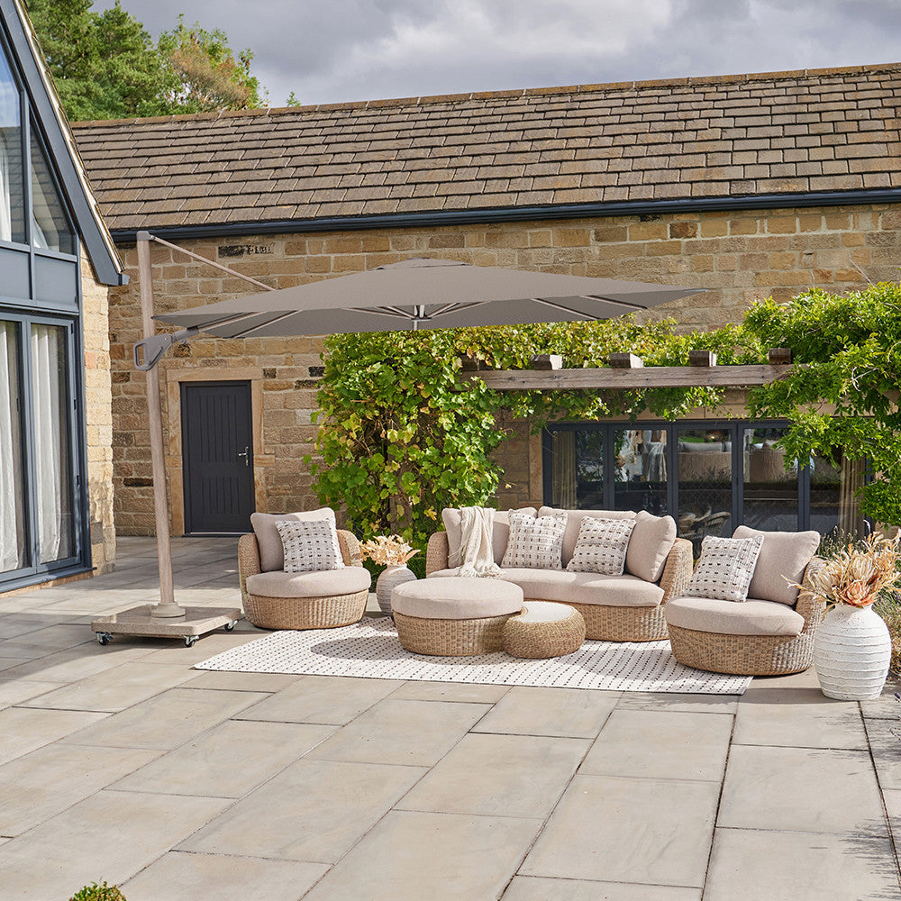 Outdoor patio area with a sectional sofa, armchairs, ottomans, and a large umbrella in front of a stone building.