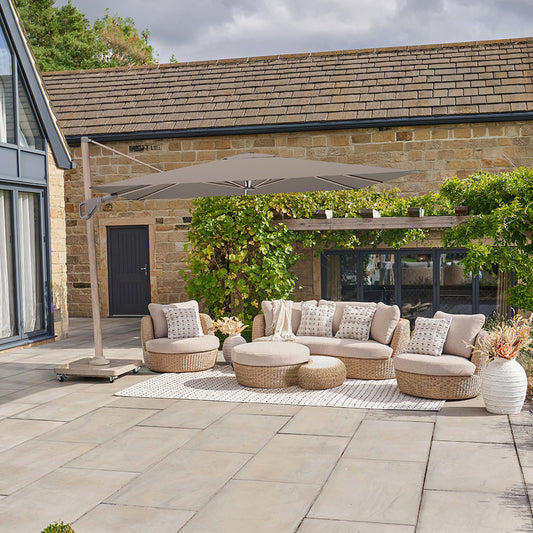 Outdoor patio area with a sectional sofa, armchairs, ottomans, and a large umbrella in front of a stone building.
