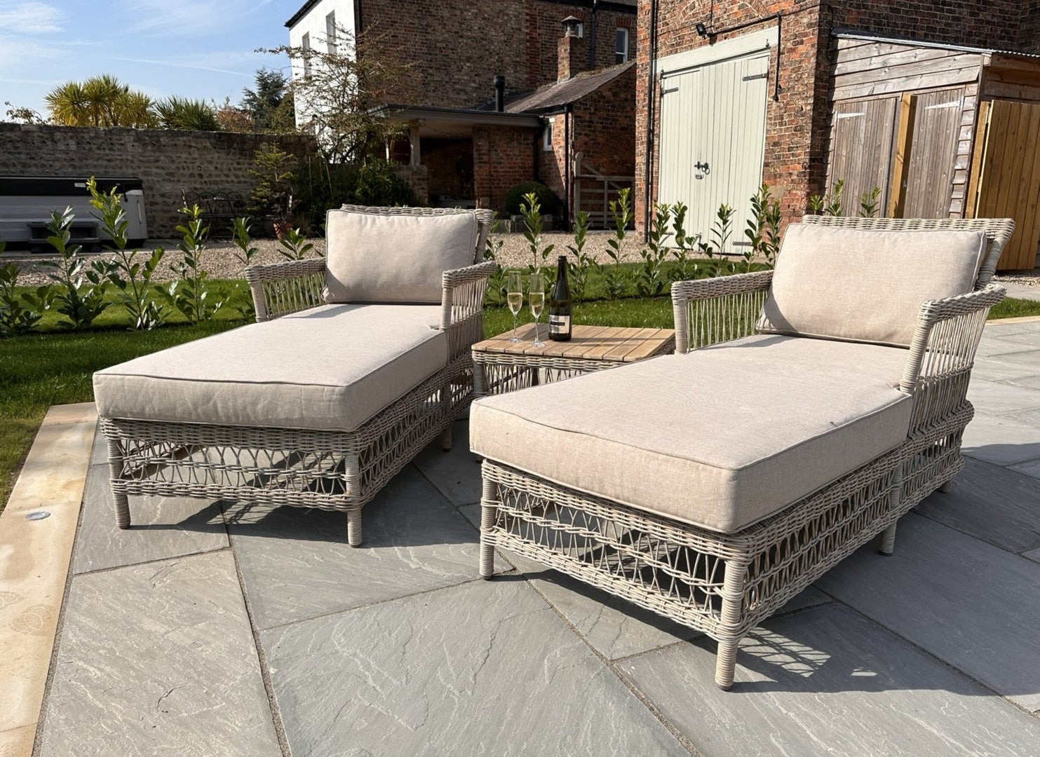 Two wicker outdoor lounge chairs with beige cushions on a stone patio.