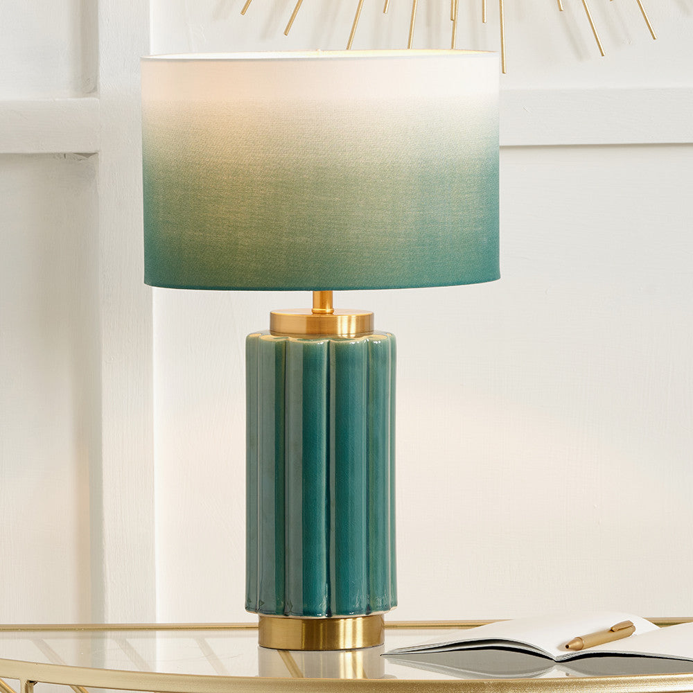 Green table lamp with gold base on a white surface