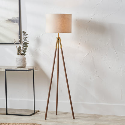 Wooden tripod floor lamp with beige lampshade in a room setting.