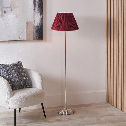 Floor lamp with a red shade next to a chair in a room with abstract art on the wall.