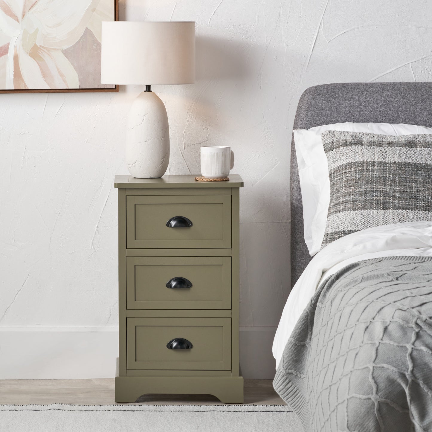 Green nightstand with a lamp and mug next to a bed with gray bedding.