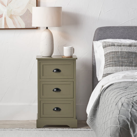 Green nightstand with a lamp and mug next to a bed with gray bedding.