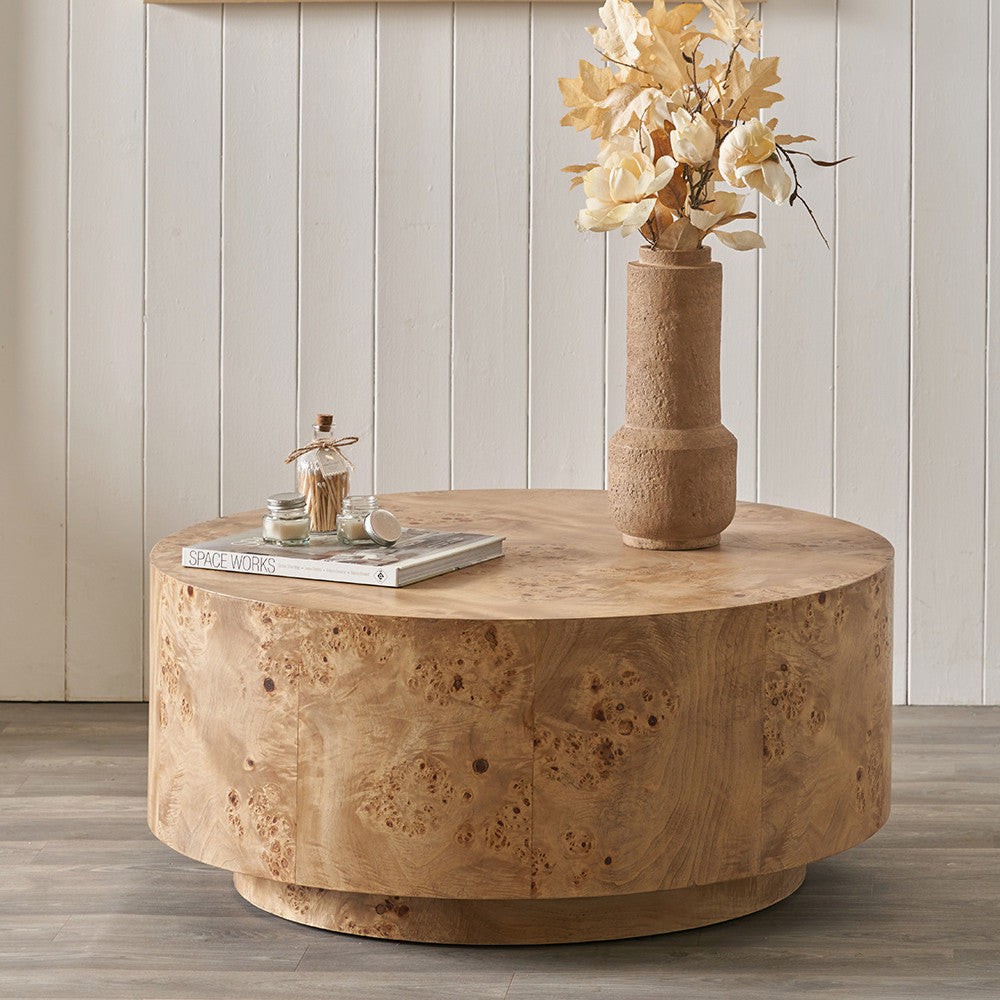 Round wooden coffee table with decorative items against a neutral wall.