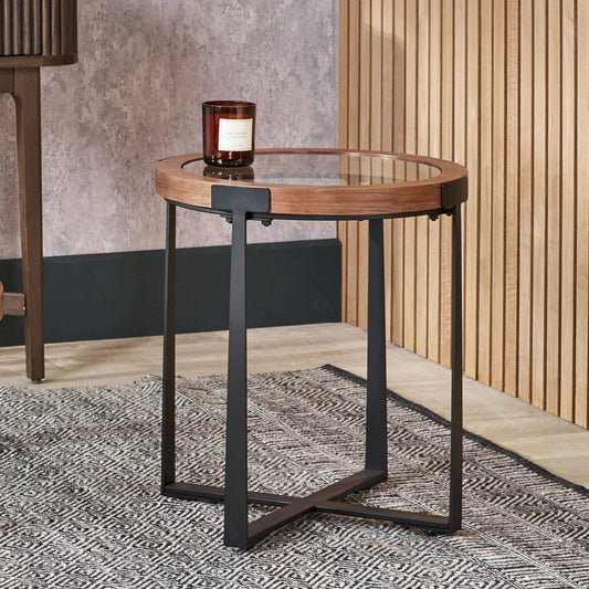 Round wooden side table with black metal legs in a room setting.