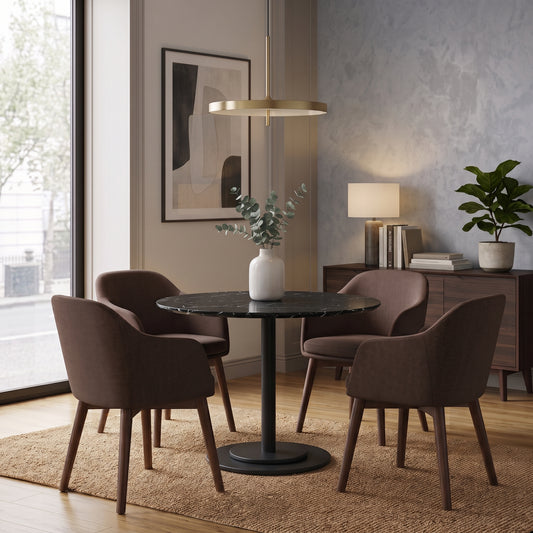 A modern dining set featuring a round black marble-top table with a black pedestal base, surrounded by four upholstered dining chairs in a warm brown fabric. The set is styled in a contemporary dining room with a wooden sideboard, a lamp, and a vase of greenery.
