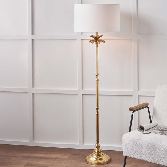 Gold floor lamp with a white shade in a room with a chair and wooden floor.