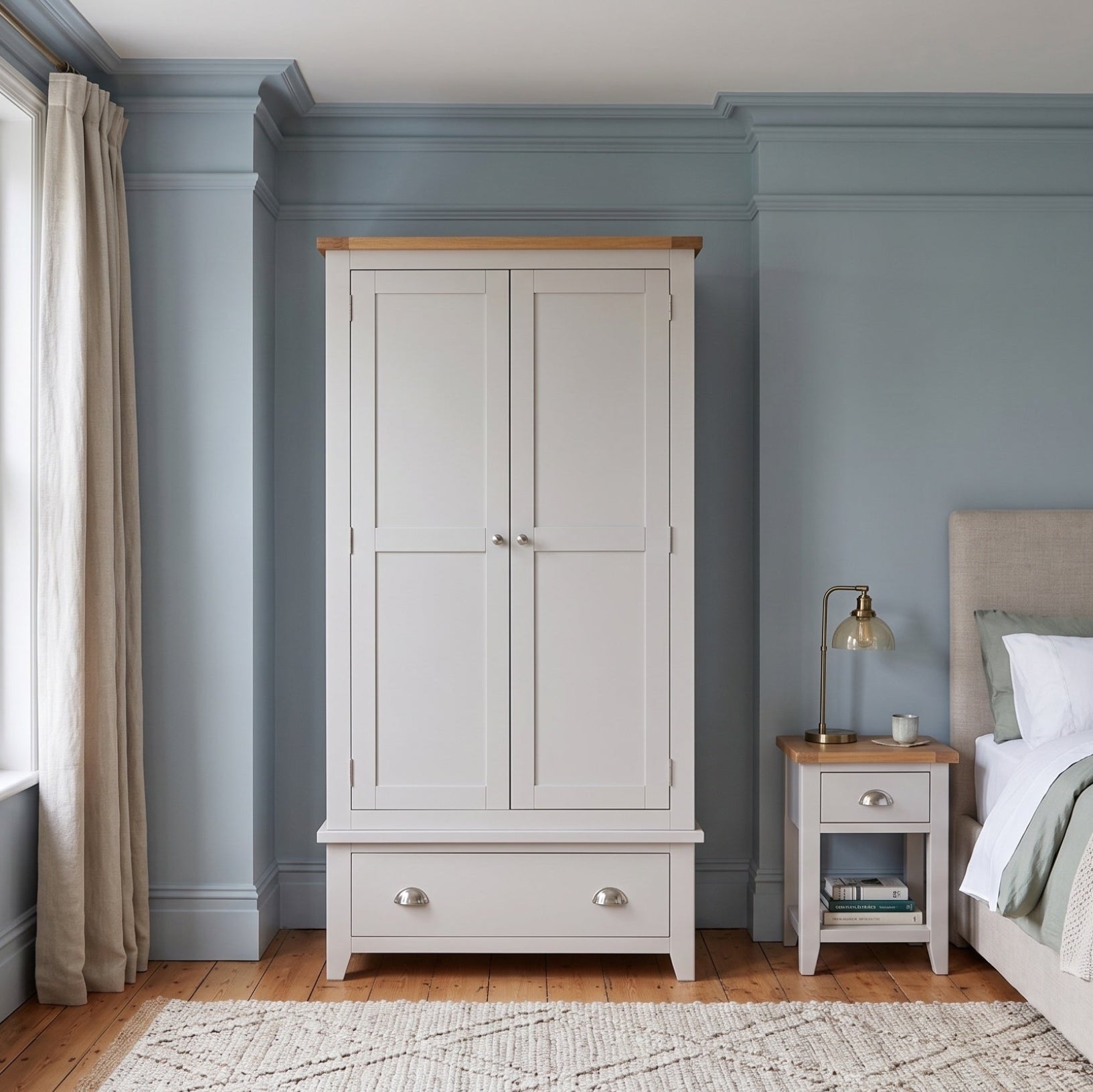 A white double-door wardrobe with a light wood top and silver knobs, positioned in a styled bedroom with blue walls, a window, and a bed.