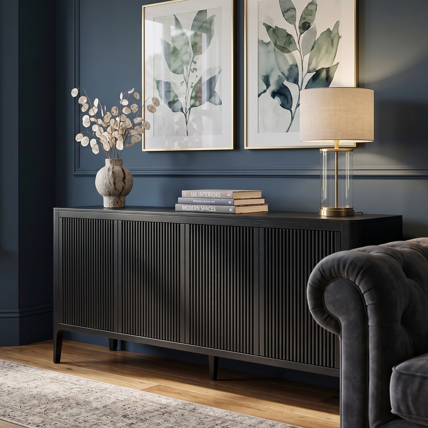 A dark wood sideboard or credenza in a styled living room corner, featuring a pleated front, styled with books, a vase of branches, and a table lamp.