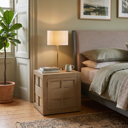 Cozy bedroom with a bed, nightstand, lamp, and plant.