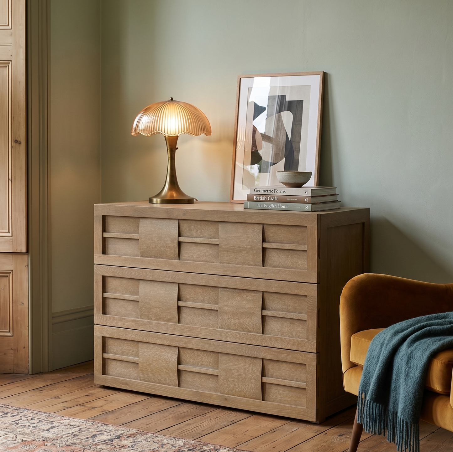 Wooden dresser with a lamp and decor items in a room with a chair and plant.
