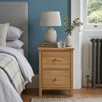 Wooden nightstand with lamp and books next to a bed in a bedroom with blue walls.