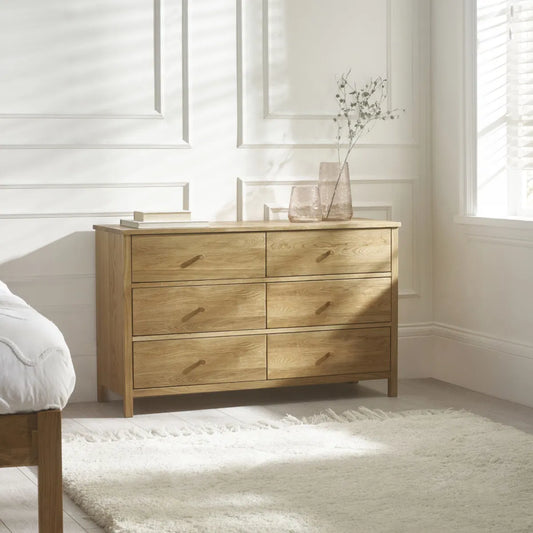 Wooden dresser in a bright bedroom with white walls and a bed.