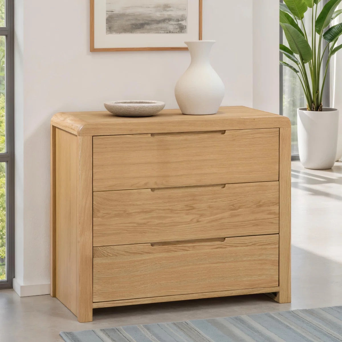 Wooden dresser with two drawers in a room with a plant and framed picture.