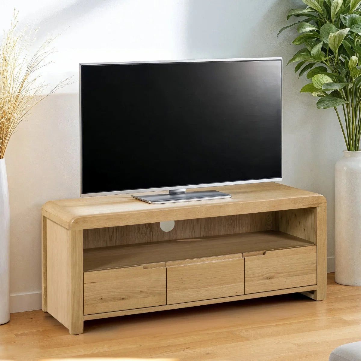 Wooden TV stand with a television on top in a room with plants and decor.