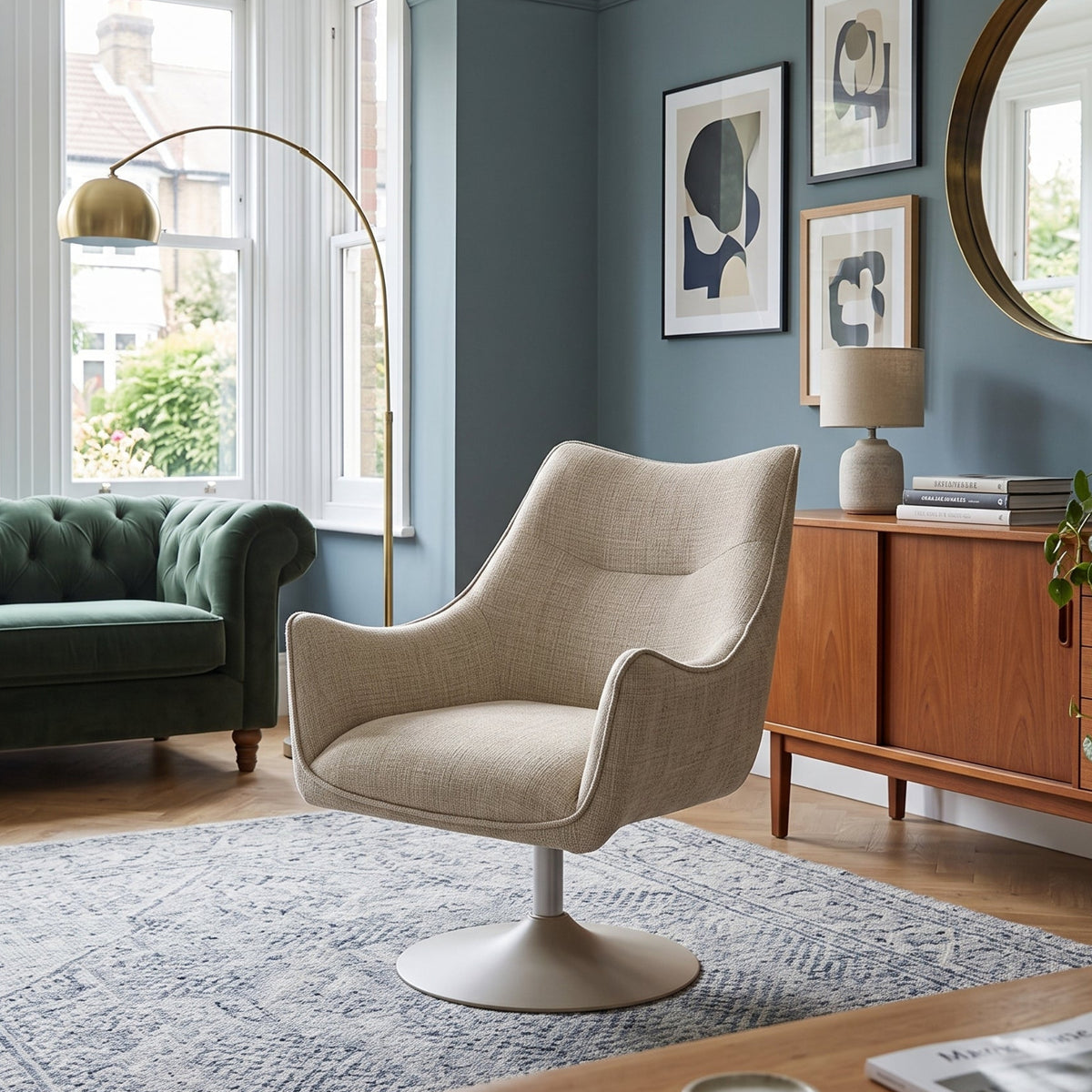 A modern beige upholstered swivel armchair with a white pedestal base, styled in a beautifully decorated living room with a green sofa, wooden credenza, and blue walls.