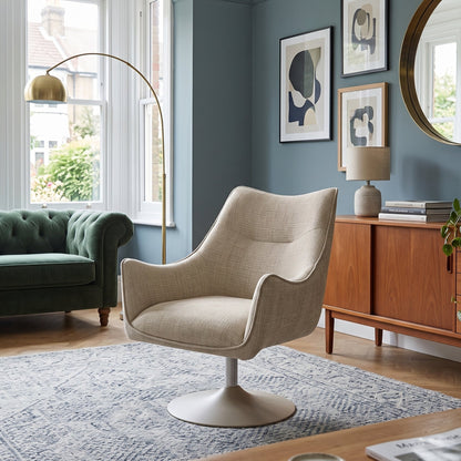 A modern beige upholstered swivel armchair with a white pedestal base, styled in a beautifully decorated living room with a green sofa, wooden credenza, and blue walls.