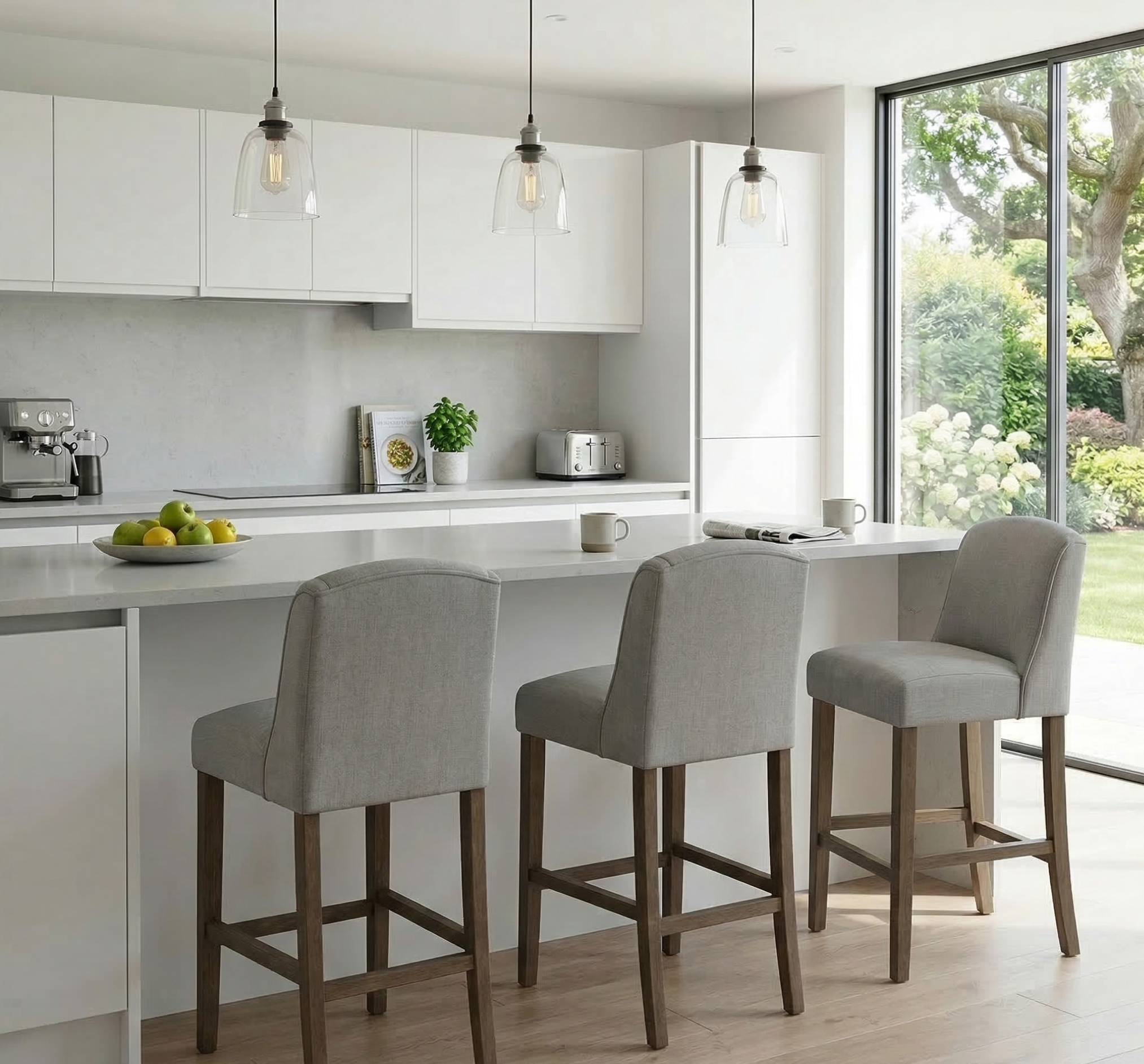 Modern kitchen with white countertops, gray bar stools, and a view of greenery outside.