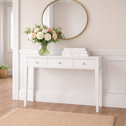 White console table with a vase of flowers and books against a beige wall.