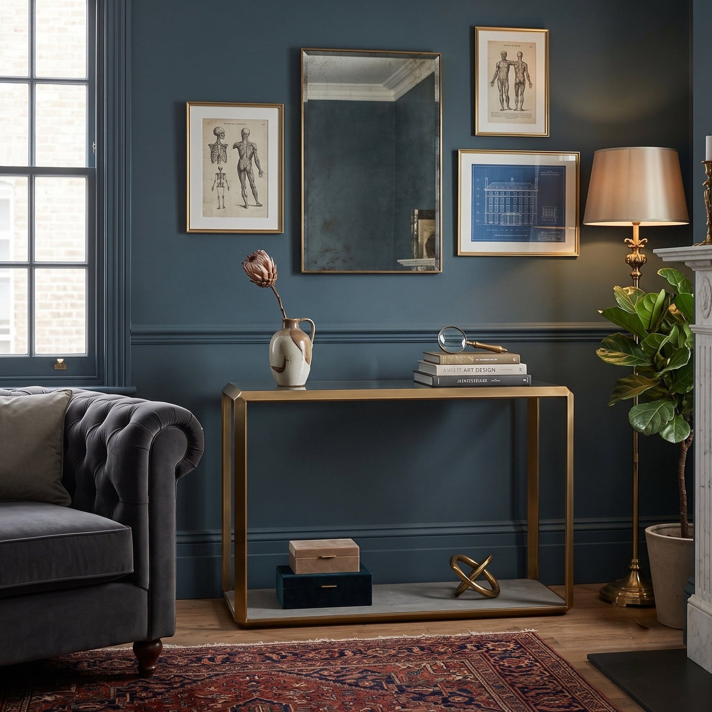 A styled interior scene with a gold-framed console table against a dark blue wall, surrounded by framed art, a mirror, a lamp, a plant, a sofa, and a rug.