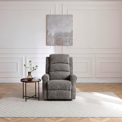 A grey upholstered recliner chair sits on a white area rug in a bright room with white paneled walls, a small round side table, and a light wood herringbone floor.