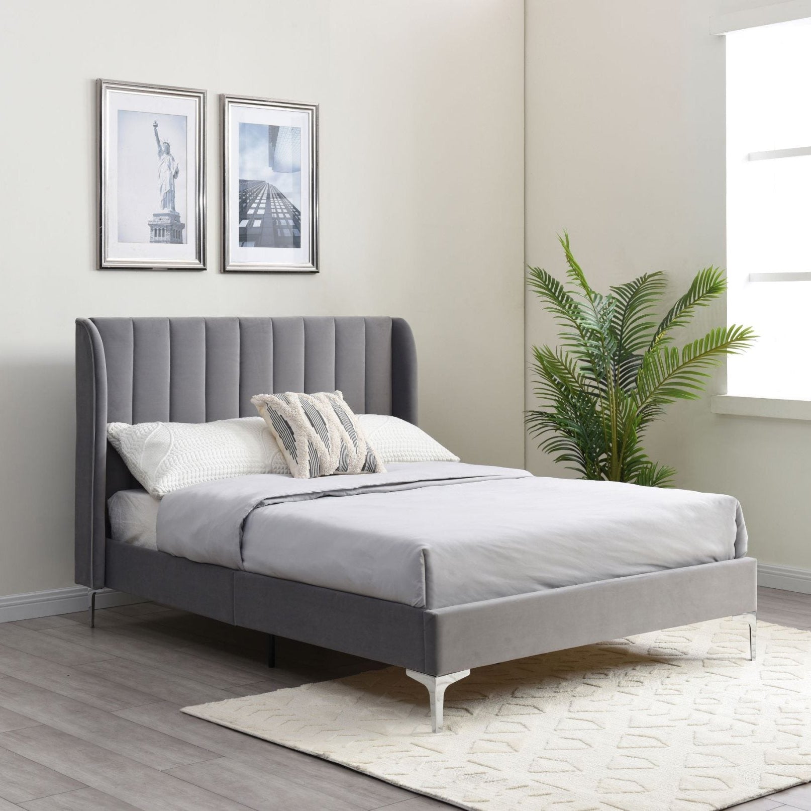 Gray upholstered bed in a bedroom with framed pictures and a plant.