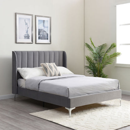 Gray upholstered bed in a bedroom with framed pictures and a plant.