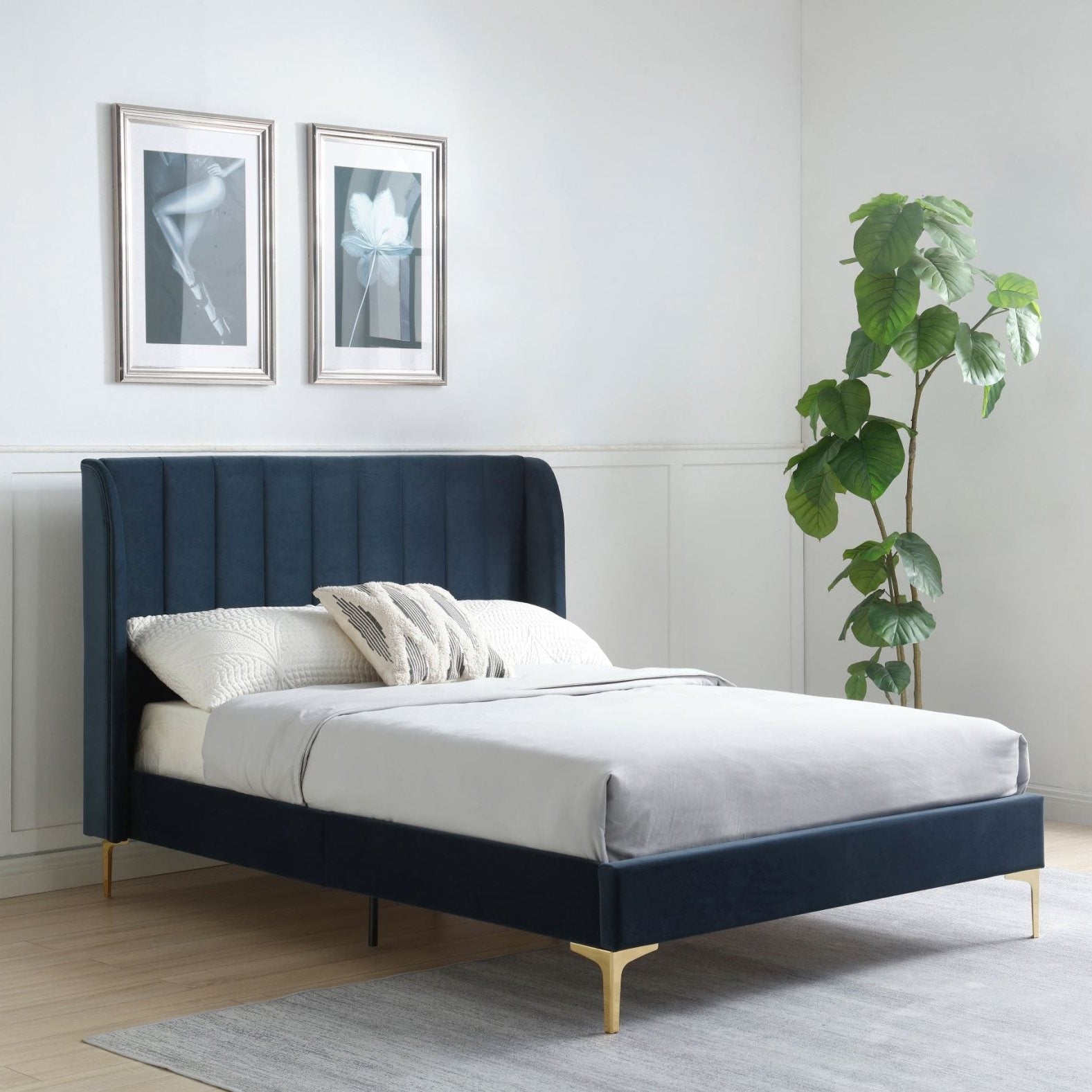 A modern upholstered bed with a deep navy blue headboard and matching footboard, styled with white bedding and gold legs in a bright, minimalist bedroom.