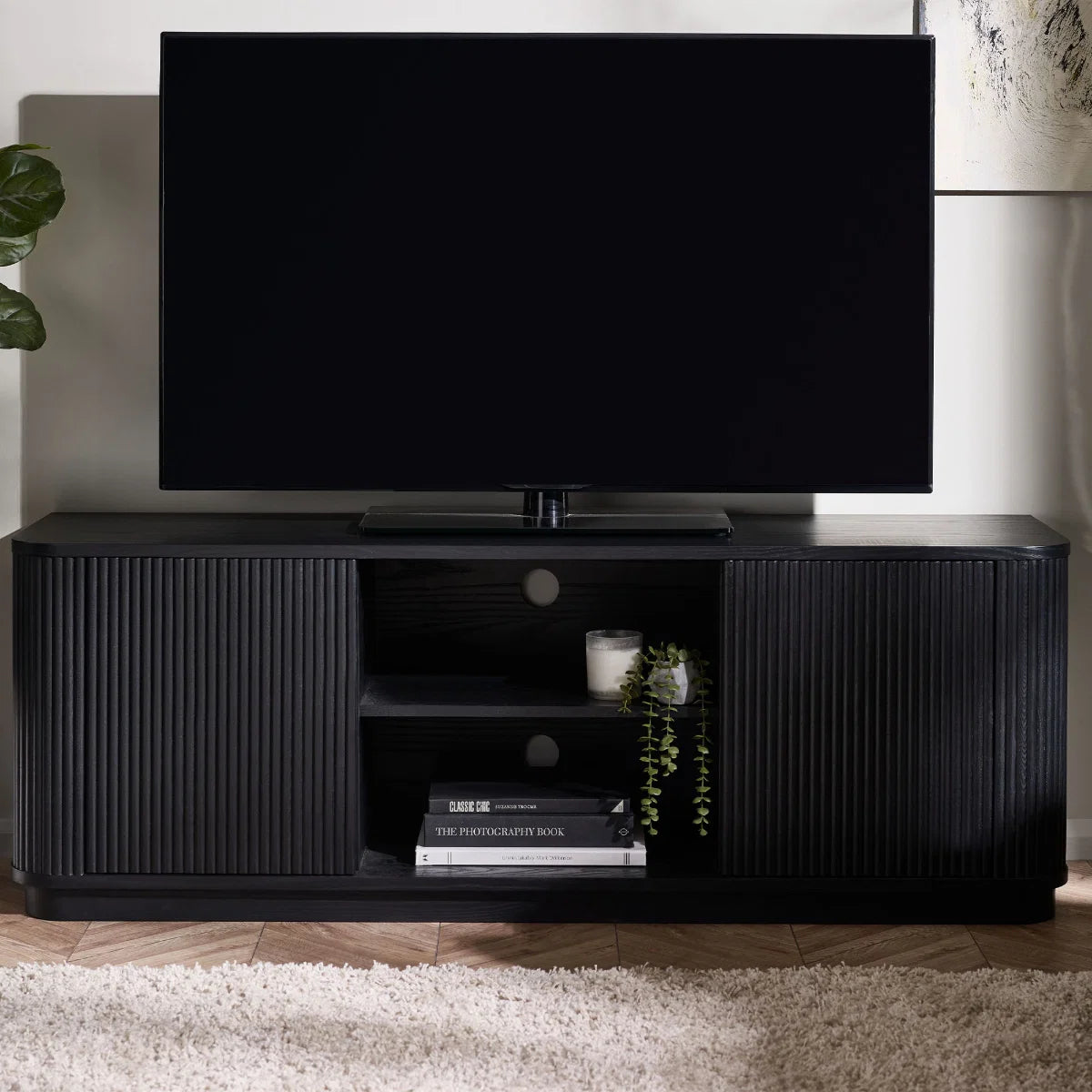 Black TV stand with a television on top in a room setting.