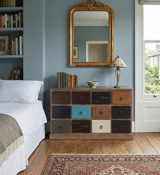 Wooden dresser with colourful drawers in a bedroom setting.