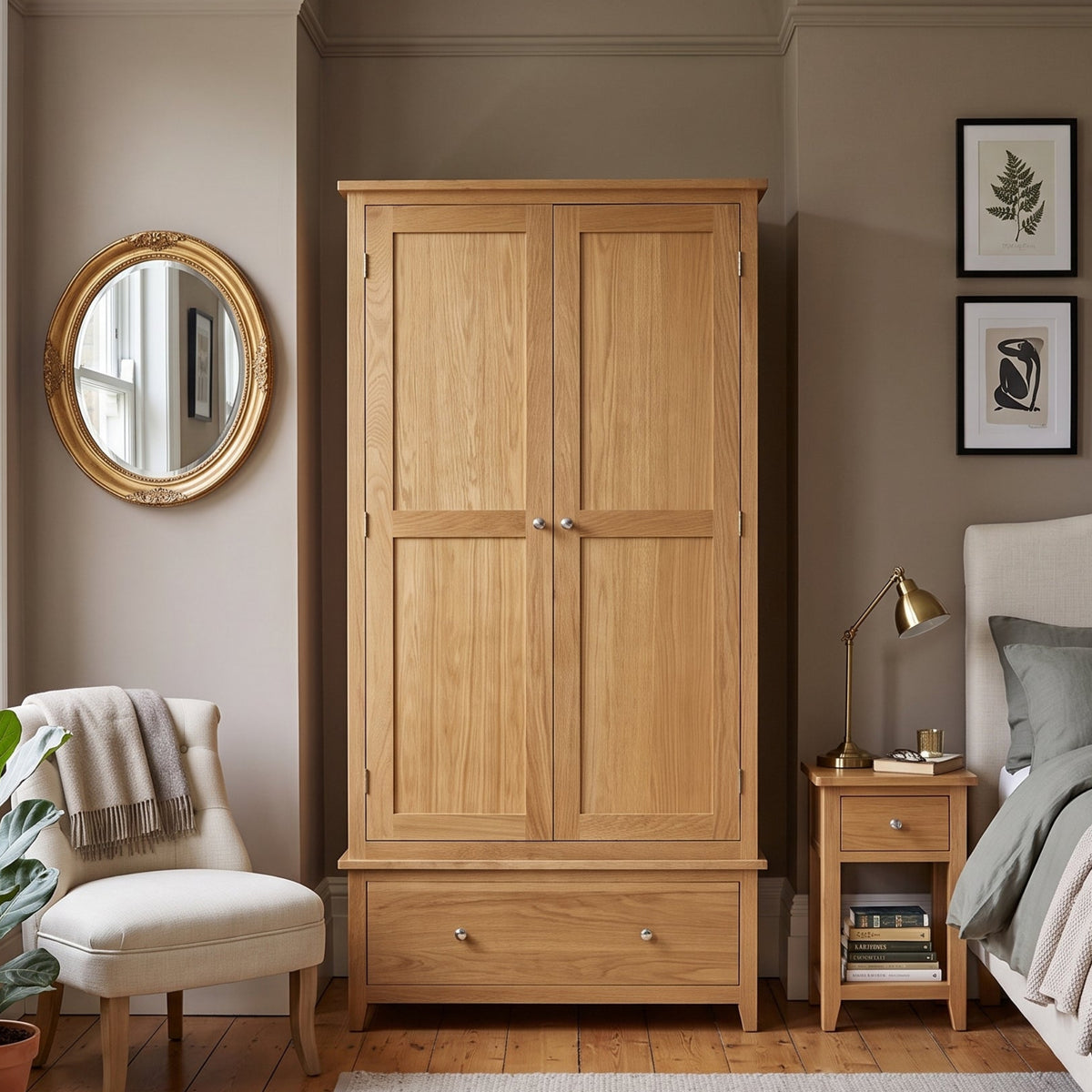 A light oak double-door wardrobe with a single drawer beneath, shown in a styled bedroom setting next to a bed and nightstand.