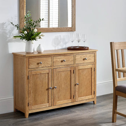 Wooden sideboard with floral arrangement and wine glasses in a dining room setting.