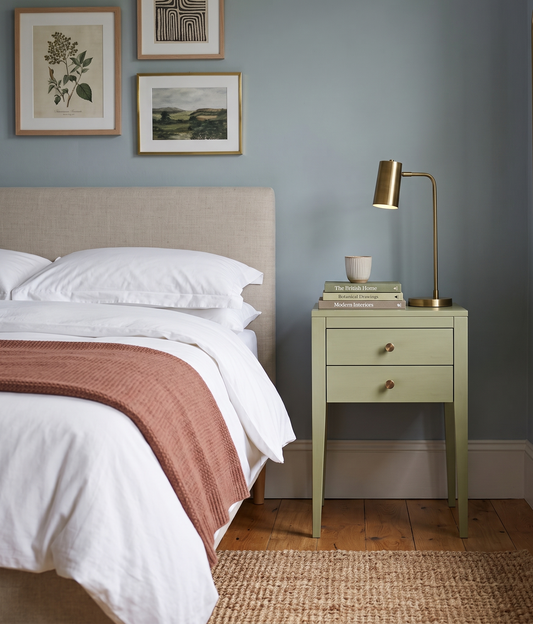 Neatly made bed with a nightstand and lamp in a bedroom setting.