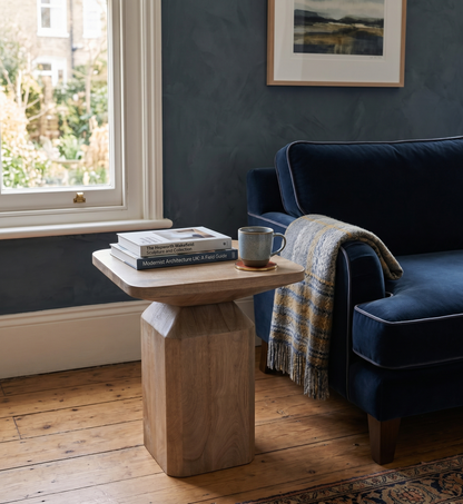 Navy blue sofa with a wooden side table and books in a room with a window and framed picture on the wall.