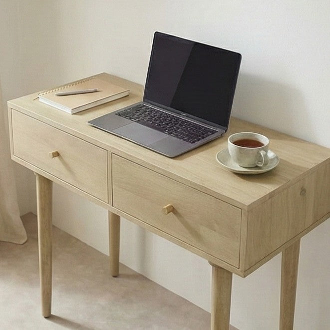 Wooden desk with a laptop, notebook, and cup of tea on a plain background