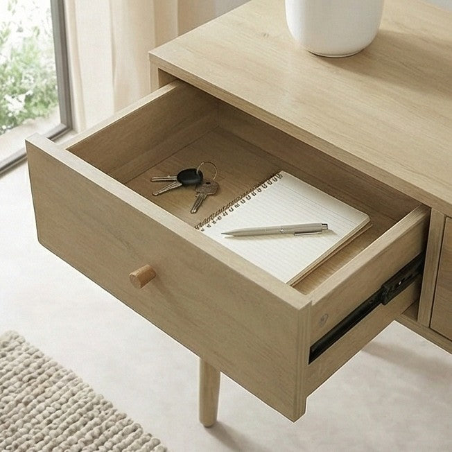 Wooden desk with open drawer containing a notebook, pen, and keys, in a bright room.