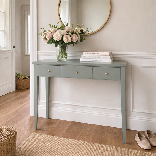 Gray console table with flowers and books in a room with wooden flooring and a mirror on the wall.