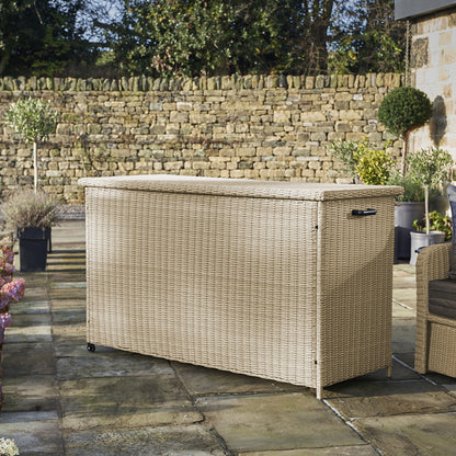 Wicker outdoor storage box on a patio with stone wall and plants in the background