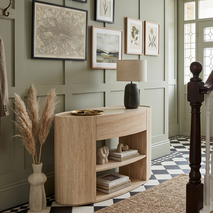 Narrow wooden console table against a wall with framed pictures in a room with checkered floor and staircase.