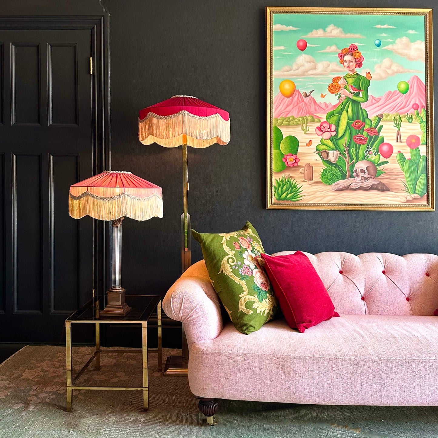 Living room with pink sofa, colorful pillows, and decorative lamps against a dark wall with a framed artwork.