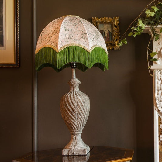 Decorative lamp with a striped green and white shade on a wooden surface next to a fireplace.